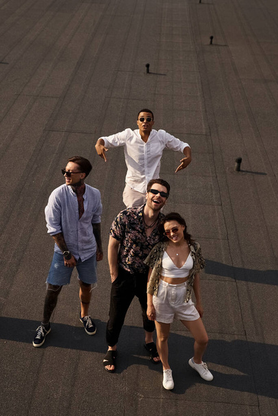 joyous diverse friends with stylish sunglasses posing on rooftop together and looking at camera - Foto, Bild