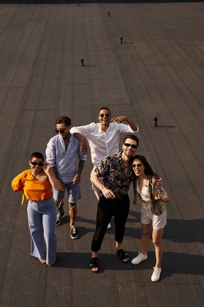 five multiracial cheerful friends in vibrant attires posing on rooftop and smiling happily at camera - Valokuva, kuva