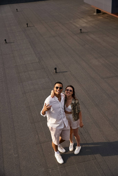 appealing diverse man and woman with sunglasses in vibrant casual attire smiling happily at camera - Foto, afbeelding