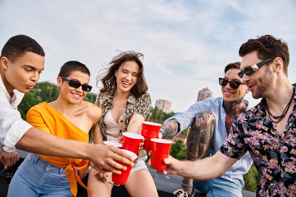 joyous multiracial friends with sunglasses clinking their red cups with drinks while on rooftop - 写真・画像