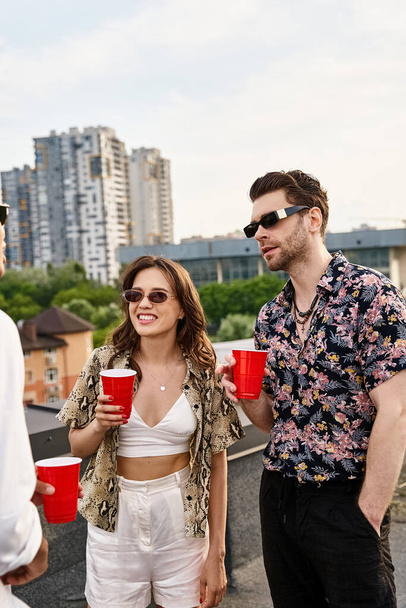 good looking jolly diverse friends with red cups with drinks talking happily at rooftop party - Фото, изображение