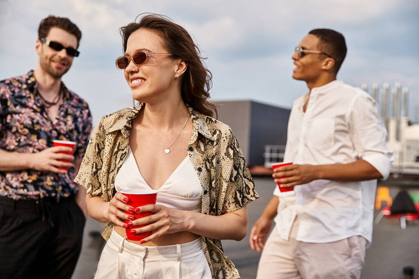 joyous woman in vibrant attire surrounded by her diverse jolly male friends at rooftop party - 写真・画像