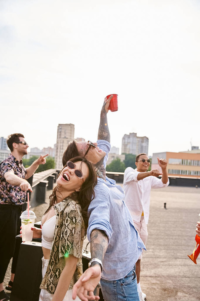 happy interracial friends with sunglasses drinking cocktails at rooftop party and chilling to DJ set - 写真・画像