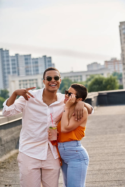 alegre interracial hombre y mujer en casual atuendos escalofriante en la azotea fiesta con cócteles - Foto, imagen