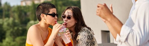 mujeres alegres bebiendo de una taza de plástico al lado de un amigo afroamericano en la fiesta de la azotea, pancarta - Foto, Imagen