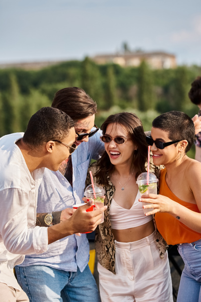 χαρούμενες πολυφυλετικές φίλες με μοντέρνα γυαλιά ηλίου πίνοντας κοκτέιλ δίπλα στον DJ στο πάρτι στην ταράτσα - Φωτογραφία, εικόνα