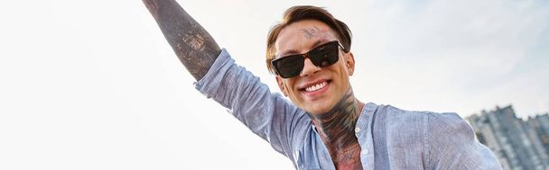 attraente uomo allegro con occhiali da sole in abbigliamento urbano sorridente felicemente alla macchina fotografica alla festa, banner - Foto, immagini