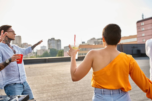 short haired young woman with cocktail in hand partying on rooftop with her tattooed friend - 写真・画像