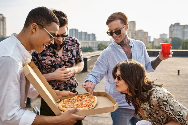 ピザをシェアするスタイリッシュなサングラスとの楽しい異人種間の友人と屋上パーティーで楽しむ - 写真・画像