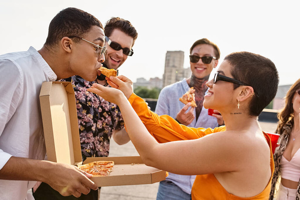 многорасовые радостные люди в модных солнцезащитных очках едят пиццу и пьют коктейли на вечеринке - Фото, изображение