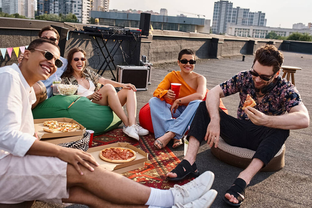 joyful multicultural friends in vibrant attires with sunglasses enjoying pizza and drinks at party - Foto, Bild