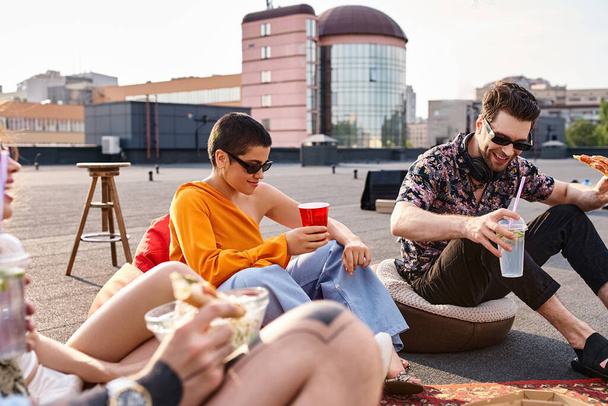attractive jolly friends in urban attires sitting on rooftop eating pizza and drinking cocktails - Фото, изображение