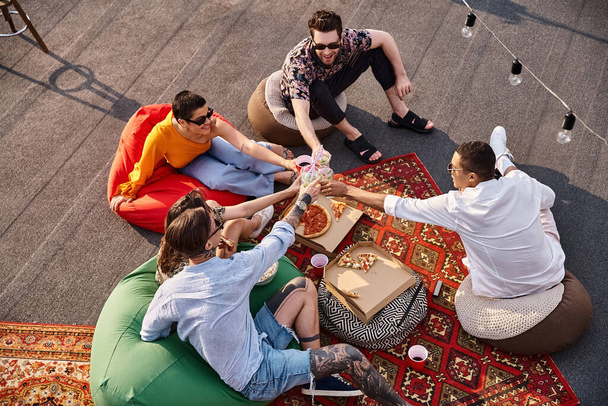 Blick von oben auf fünf verschiedene lustige Freunde, die bei einer Dachparty Pizza und klappernde Tassen mit Getränken genießen - Foto, Bild
