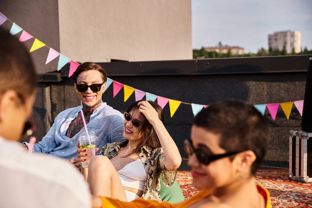 radosnych, atrakcyjnych przyjaciół z modnymi okularami przeciwsłonecznymi siedzących na dachu i pijących koktajle na imprezie - Zdjęcie, obraz