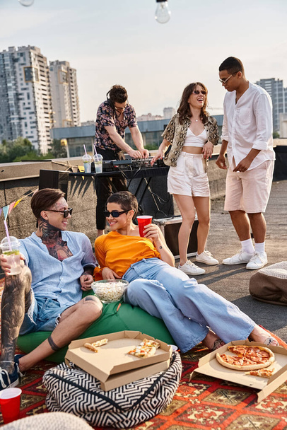 pessoas alegres multiculturais em trajes vibrantes urbanos desfrutando de festa no telhado com música e bebidas - Foto, Imagem