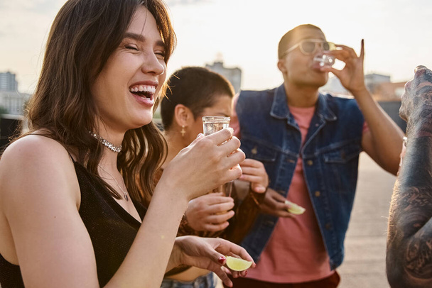 joyful multicultural people in vibrant clothing enjoying tequila with salt and lime at rooftop party - 写真・画像