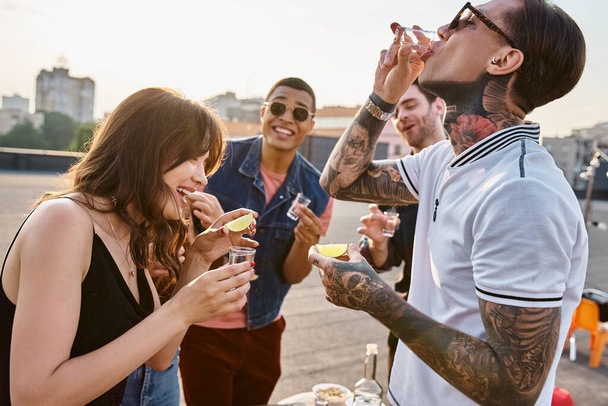 fröhliche multikulturelle Menschen in lebendiger Kleidung genießen Tequila mit Salz und Kalk auf einer Dachparty - Foto, Bild