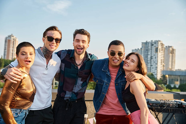 good looking jolly multiracial friends posing together on rooftop and smiling happily at camera - Photo, image