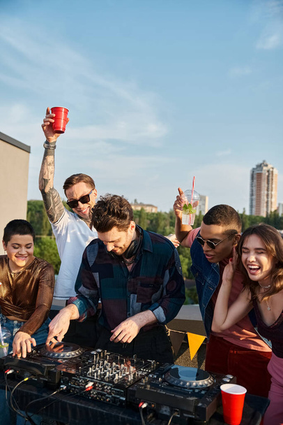 Diverse gut gelaunte Menschen in lebendigen Outfits feiern zusammen neben einem gutaussehenden DJ auf einer Dachparty - Foto, Bild