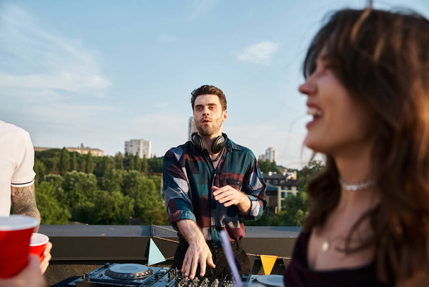 Fokus auf gutaussehenden fröhlichen DJ, der Musik für seine verschwommenen fröhlichen Freunde auf Dachterrassen-Party spielt - Foto, Bild