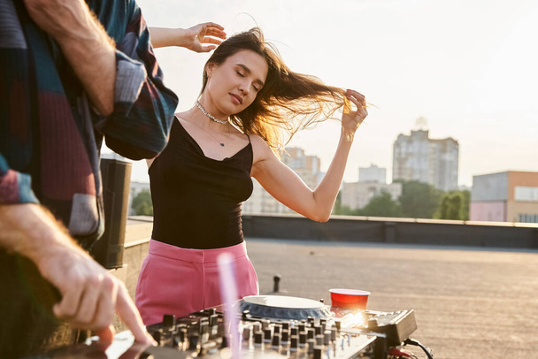 hermosa mujer de pelo largo en traje vibrante festivo posando junto a DJ durante la fiesta en la azotea - Foto, Imagen