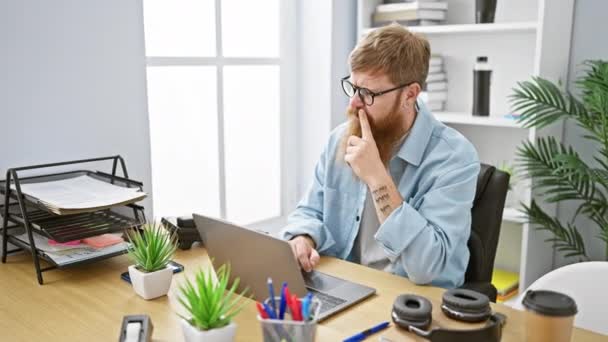Kendine güvenen genç kızıl saçlı adam ofisteki laptopta neşeli bir şekilde çalışıyor, iş adamı olarak kendine güveniyor. - Video, Çekim
