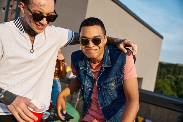 радісні мультикультурні чоловіки в яскравому повсякденному вбранні тримають коктейлі і дивляться на камеру на вечірці - Фото, зображення