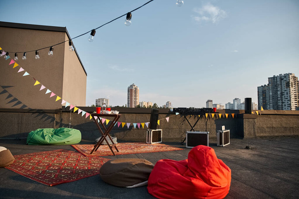 object photo of outdoor rooftop with red carpets and DJ equipment with plates and cups on table - Photo, Image