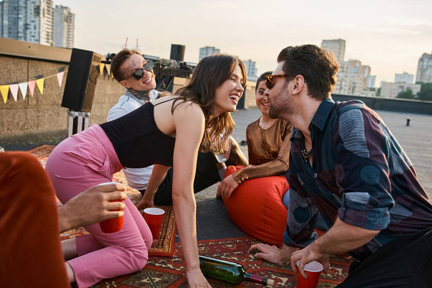 νεαροί χαρούμενοι άνθρωποι με αστικά ρούχα που παίζουν στριφογυρίζουν το μπουκάλι μαζί στην ταράτσα, πρόκειται να φιληθούν - Φωτογραφία, εικόνα