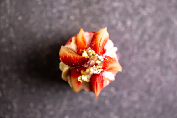 Eine Nahaufnahme einer Erdbeer-Sahne-Torte mit Blattgold auf einem Tisch aus dunklem Stein. Hergestellt mit frischen Erdbeeren, Sahne, buttriger Kruste. - Foto, Bild