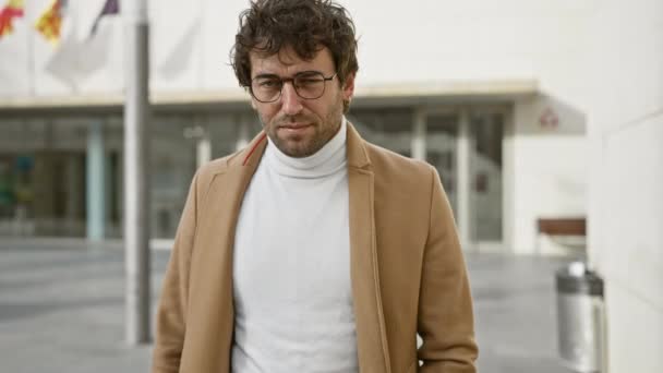 Magabiztos spanyol férfi, szakállas szemüveggel és kabátban pózol a város utcáján.. - Felvétel, videó