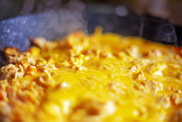 Cocine una tortilla caliente con tomates y trozos de pollo en una sartén bajo una tapa abierta. bocadillo saludable - Foto, imagen