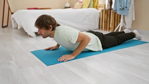 Hombre guapo practicando yoga en un amplio dormitorio, exudando calma y armonía en un entorno hogareño sereno. - Imágenes, Vídeo