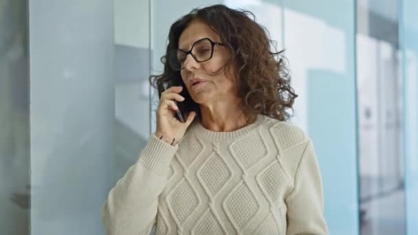 Μια ώριμη Ισπανίδα μιλάει σε ένα smartphone σε ένα σύγχρονο περιβάλλον γραφείου, αποπνέοντας επαγγελματισμό και συγκέντρωση. - Πλάνα, βίντεο