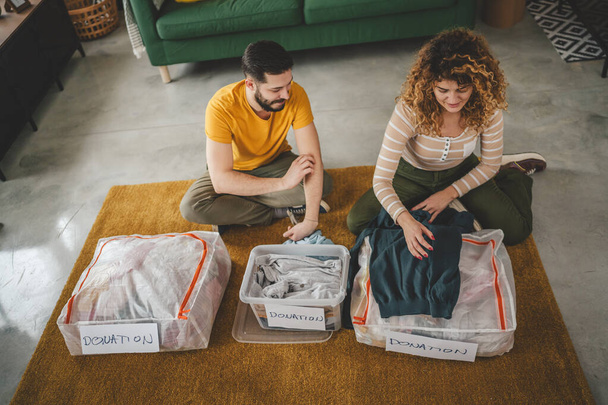 Mann und Frau Mann und Frau Ehepaar stehen zu Hause und sortieren Kleidungsstücke für die Kleiderspende in die Kartons im Wohnzimmer ihrer Wohnung - Foto, Bild