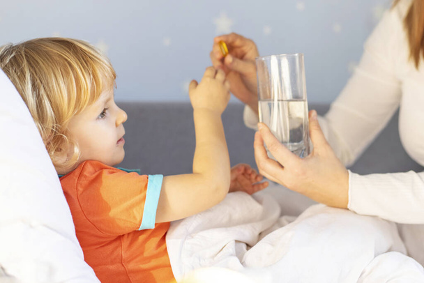 Un moment tendre comme une mère au lit donne la médecine à son tout-petit attentif, aux côtés d'un verre d'eau. - Photo, image