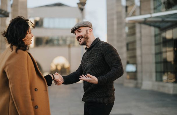 Hombre y mujer alegres estrechando las manos en el entorno urbano con sonrisas cálidas. - Foto, imagen