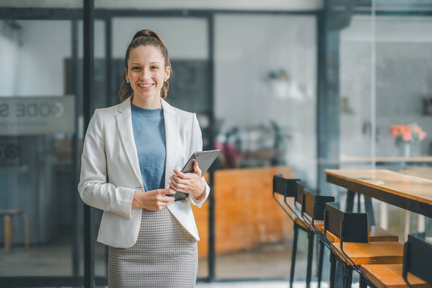Business woman koncepció, mosolygós professzionális üzletasszony kezében egy tabletta kortárs irodai környezetben, magabiztosságot és hatékonyságot árasztva. - Fotó, kép