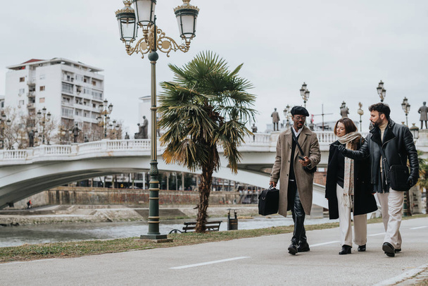 Tre professionisti ben vestiti camminano e conversano vicino a un ponte panoramico in un parco cittadino, segnalando il lavoro di squadra e lo stile di vita urbano. - Foto, immagini