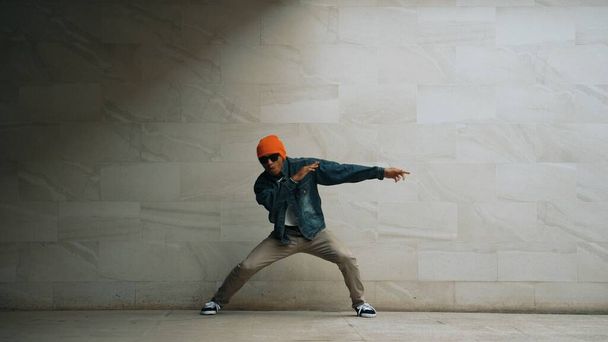 Motion shot van hipster uit te voeren break dance op grijze achtergrond. Straatdanser oefenen hip hop beweging terwijl het dragen van stijlvolle hip hop doek en verplaatsen naar funky muziek. Outdoor sport 2024. Schitterend.. - Foto, afbeelding