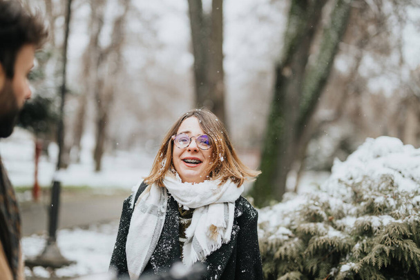 公園の穏やかな雪の中でメガネをかけた陽気な若い実業家が笑い,楽しいワークライフバランスを提案する. - 写真・画像
