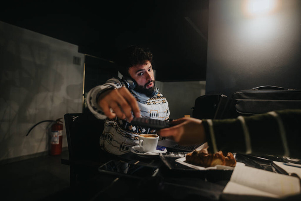 Zaměřený muž pracuje pozdě na notebook v tmavé místnosti s kávou a jídlem. - Fotografie, Obrázek