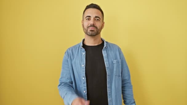 デニムシャツの陽気な若いヒスパニックの男はカメラに愛のキスを送信し,黄色の壁の背景にセクシーな自信を放射する - 映像、動画