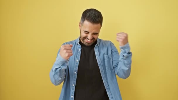 Екстатичний молодий іспаномовний чоловік у джинсовій сорочці святкує перемогу, кричачи про радість. збуджений жест переможця, що стоїть ізольовано на жовтому тлі. - Кадри, відео