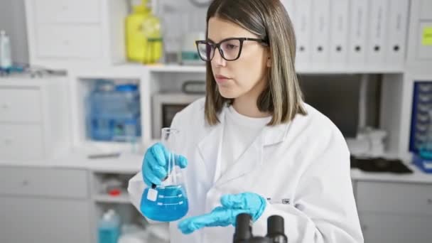 Een jonge Spaanse vrouwelijke wetenschapper analyseert een blauwe chemische oplossing in een laboratoriumomgeving, die expertise en concentratie aantoont.. - Video