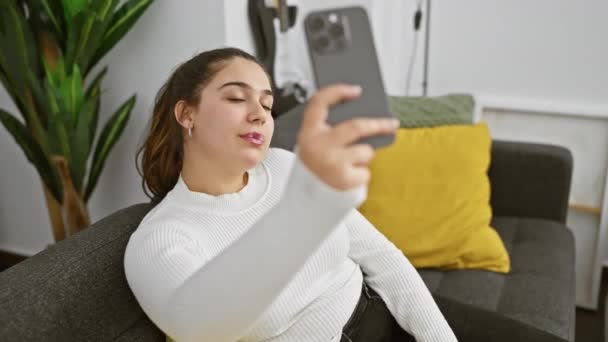 Ισπανίδα γυναίκα vaping σε εσωτερικούς χώρους, ενώ χρησιμοποιώντας το smartphone της, που περιβάλλεται από διακόσμηση στο σπίτι σε ένα άνετο διαμέρισμα ρύθμιση. - Πλάνα, βίντεο