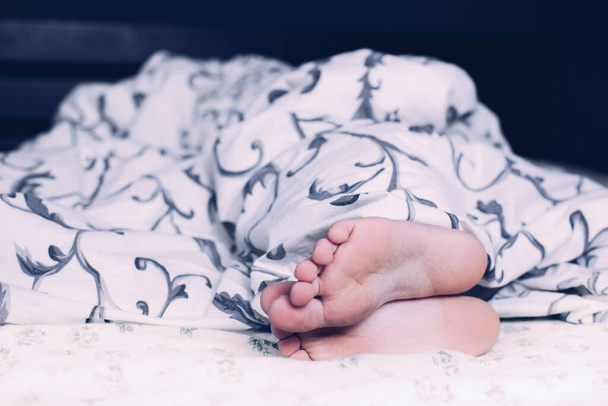 Nackte Füße eines Kindes. Das Kind schläft im Bett. Die Beine schauen unter den Decken hervor. Beine und Ferse - Foto, Bild