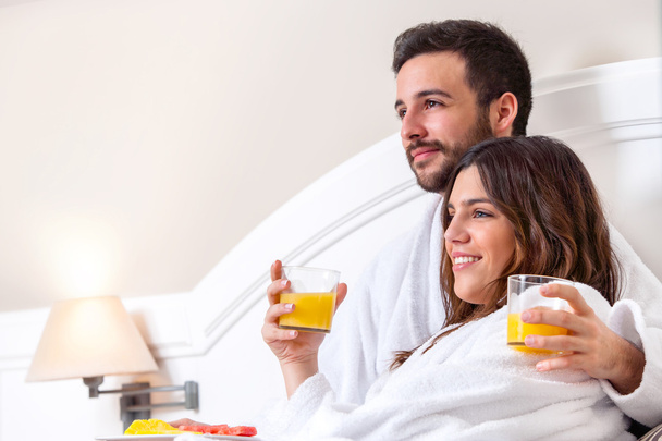 Couple in bathrobe drinking orange juice. - Фото, изображение