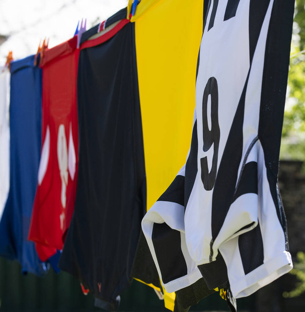 Πολύχρωμα ρούχα κρέμονται για να στεγνώσει σε μια γραμμή πλυντηρίου. φανέλες ποδοσφαίρου - Φωτογραφία, εικόνα