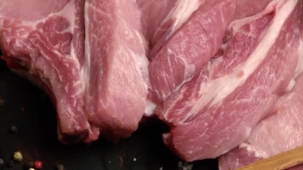 Syrové čerstvé vepřové maso nakrájené na plátky ke smažení (vepřový steak), které se otáčí na dřevěné desce kraft. Zvětšení kamery z blízka na široký záběr. Horní pohled - Záběry, video